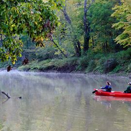 Two people paddle a red canoe on a stream.