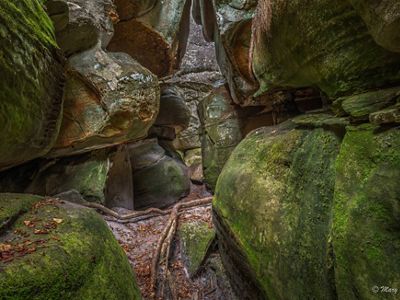 Large moss covered boulders press in close to each other creating narrow passages between them.
