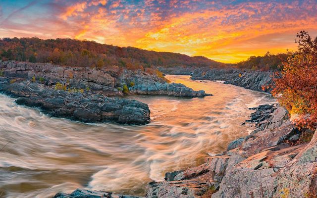 White rapids swirl and eddy as the Potomac River rushes through rocky formations at Great Falls as the sun rises.