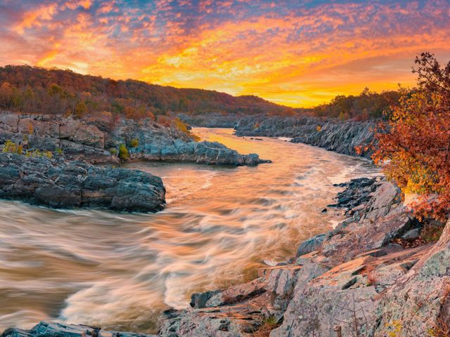 White rapids swirl and eddy as the Potomac River rushes through rocky formations at Great Falls as the sun rises.