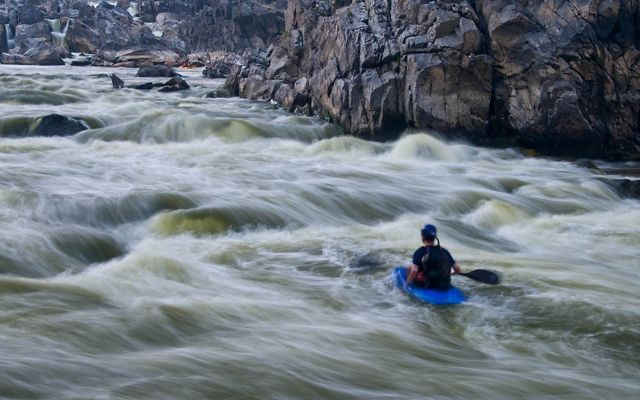 Swirling white water is a blur as it rushes past a man in a blue kayak, racing between the steep rocky sides of the channel.