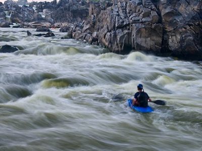 Swirling white water is a blur as it rushes past a man in a blue kayak, racing between the steep rocky sides of the channel.