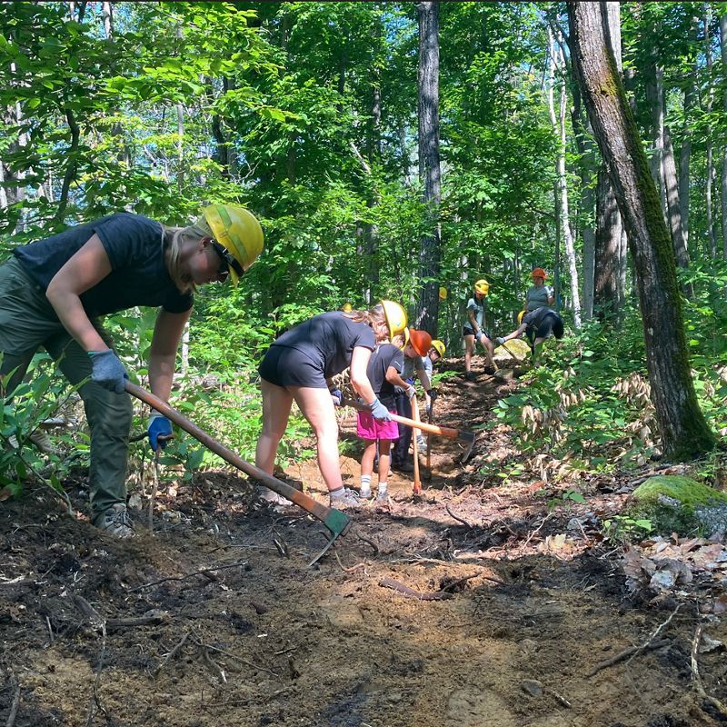 People in hard hats and tools working on a trail in the woods.
