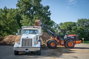 A front loader dumps soil into a waiting dump truck.