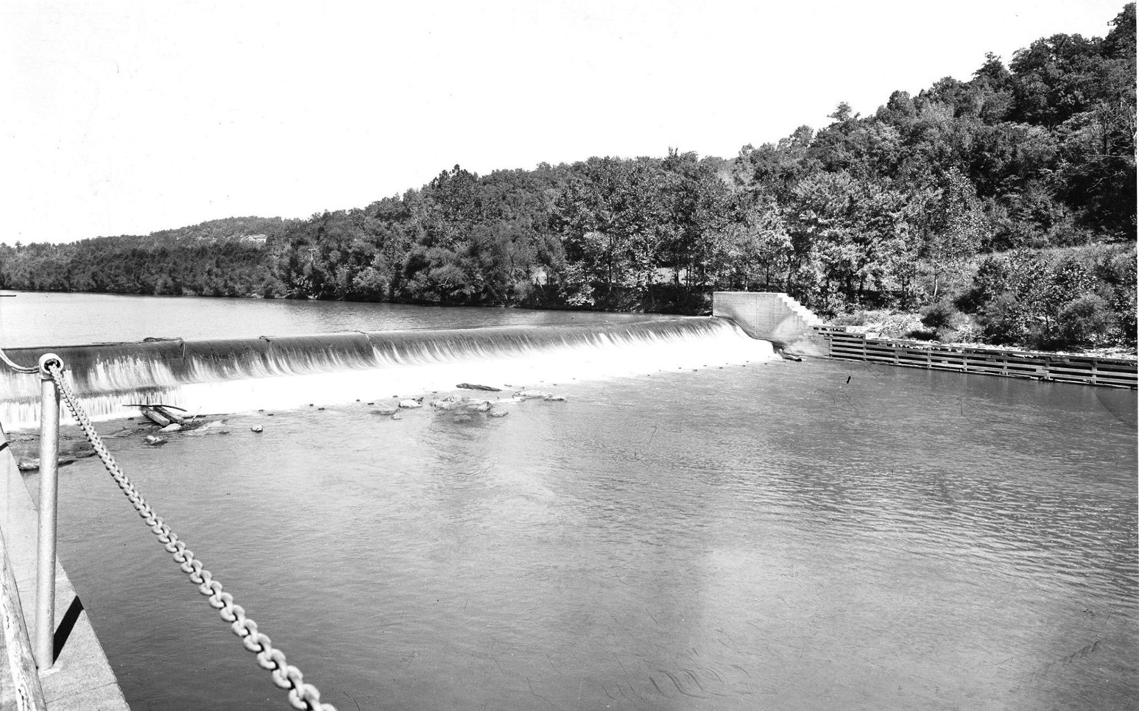 An historic image of a barge operating near a dam. 