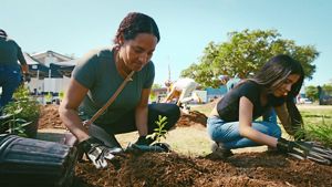 Two women kneel in the dirt planting small green seedlings.