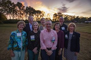 A group of people stand in front of a sunset and smile at the camera.