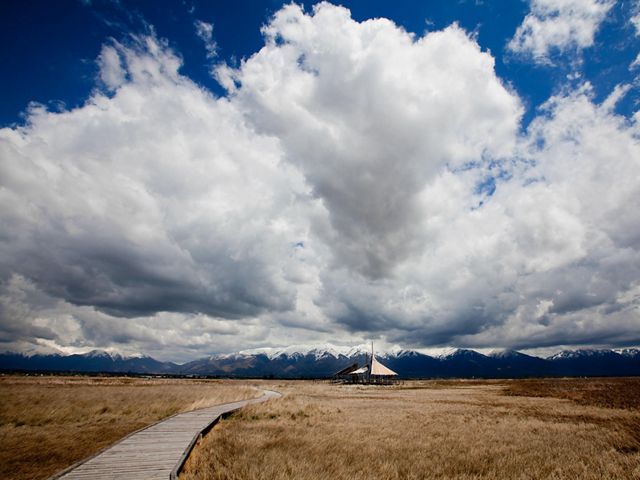 The Great Salt Lake Shorelands Preserve pavilion stands in a vast grass field under a dramatic blue sky filled with clouds.