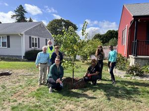 A group of people pose for a picture around a tree. 