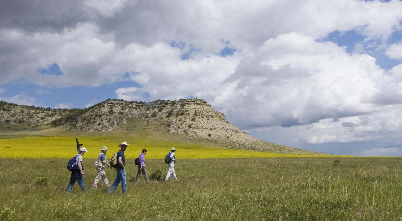 Guests hike under moody skies across a meadow at the base of Pine Butte on the Pine Butte Swamp Preserve located on the Rocky Mountain Front in Montana.