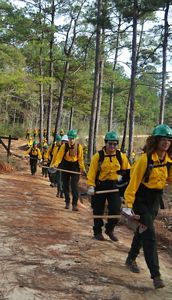 A line of corps members in fire gear walks on a trail.