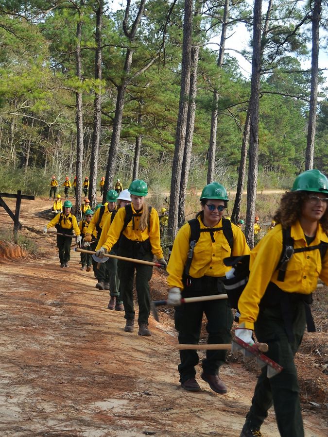 A line of corps members in fire gear walks on a trail.
