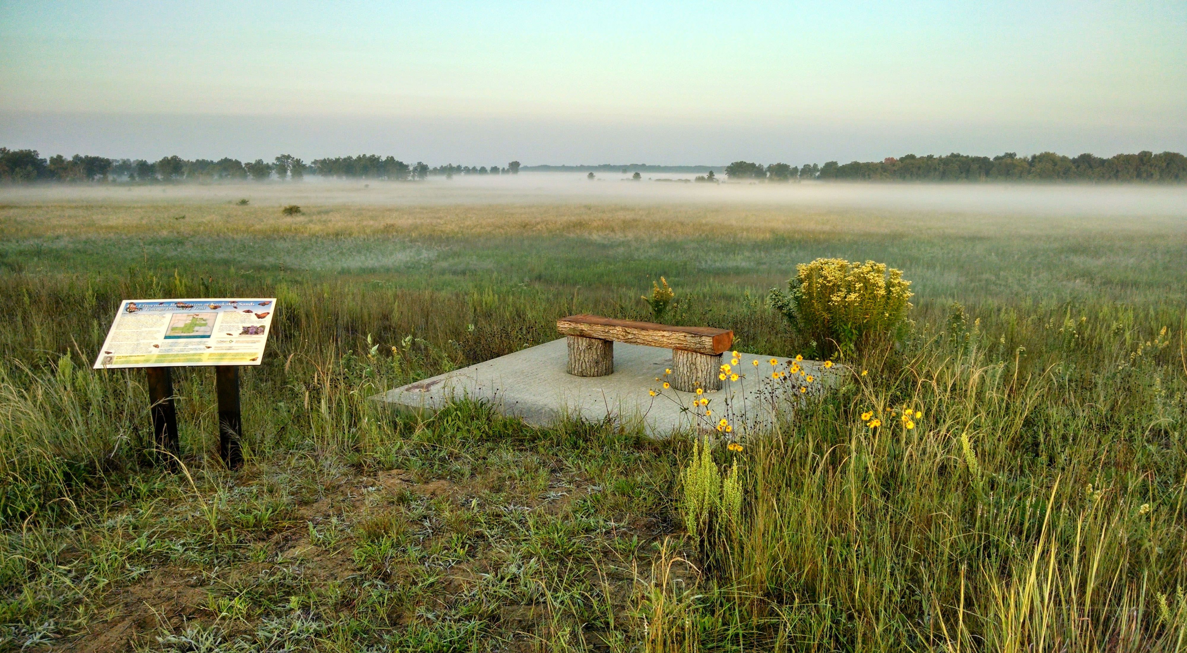 An overlook with signage and a bench looking out onto a misty prairie landscape.