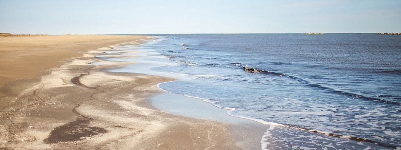 A gray ocean meets a sandy beach under blue skies.