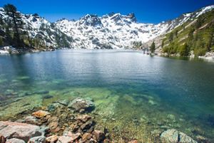 Deep blue clear water of a mountain lake situated beneath a snowy peak.