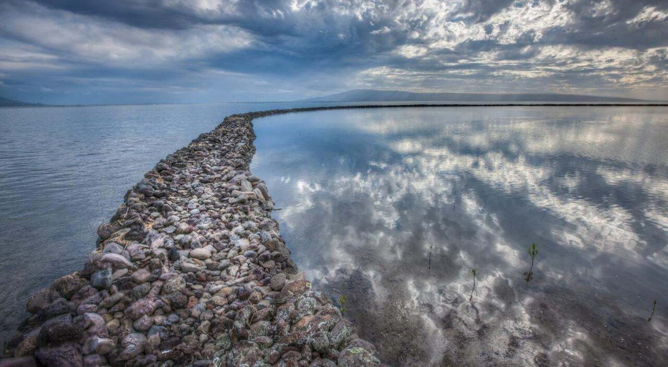 Long, curving row of rocks forms a fish pond in a large body of water.