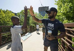 A man and a boy high-five each other on a pedestrian bridge in an urban setting.