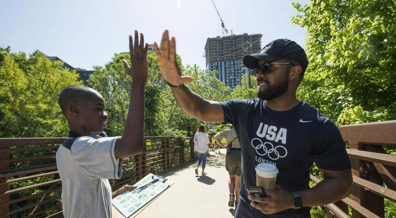 A man and a boy high-five each other on a pedestrian bridge in an urban setting.