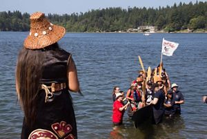 Group of people in a canoe in a bay framed by forested shoreline.