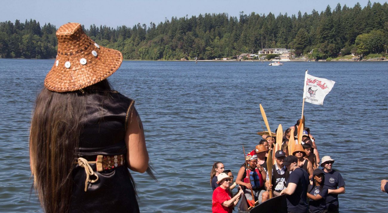 Group of people in a canoe in a bay framed by forested shoreline.