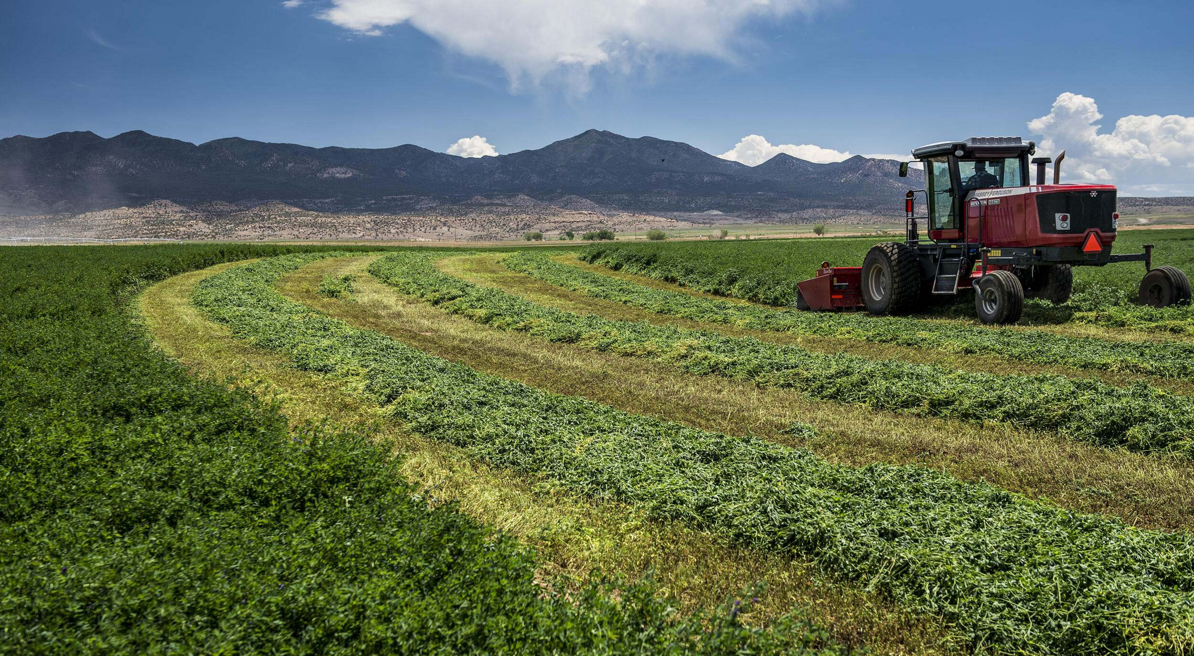 A tractor plows over farmland with mountains in the background.