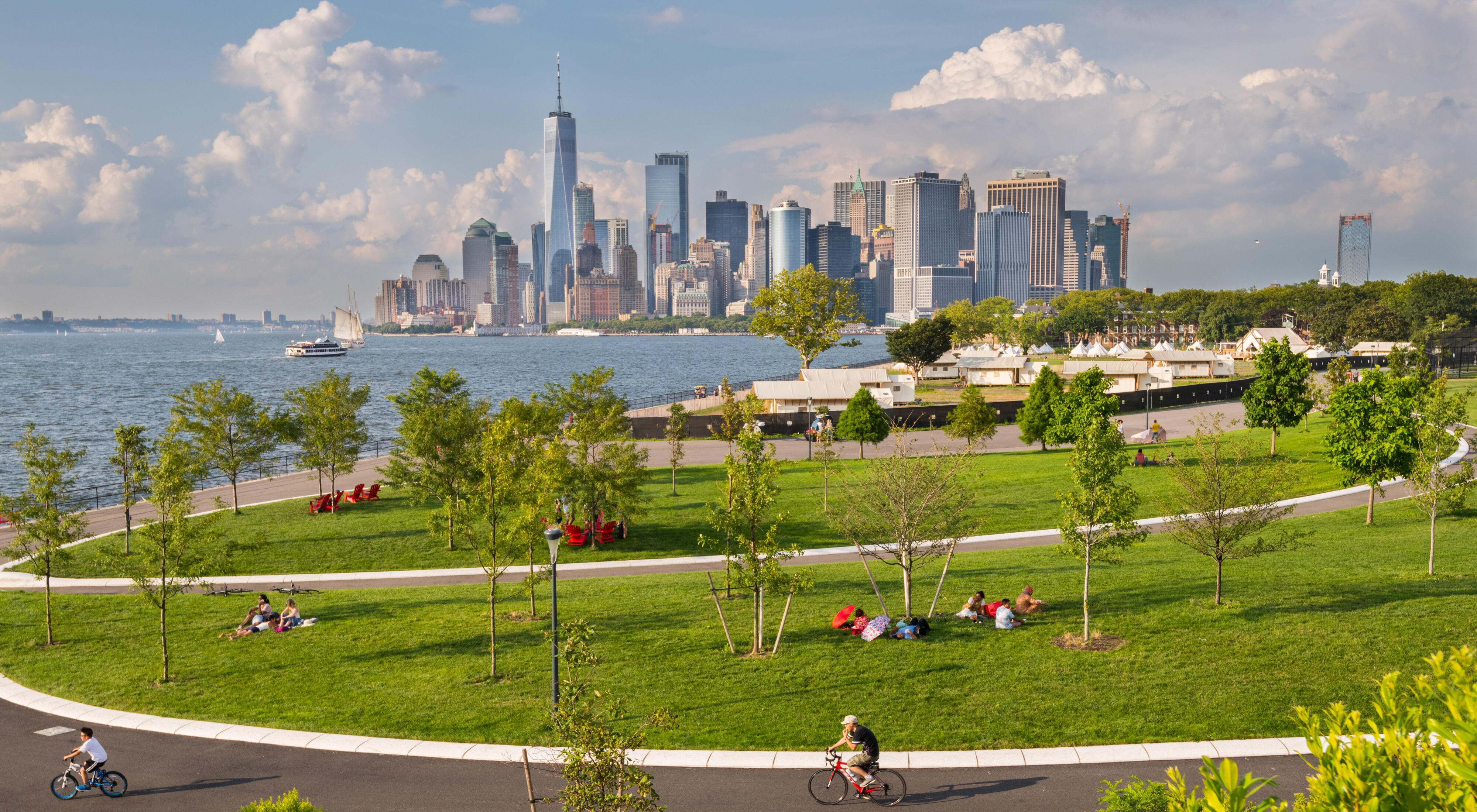 People ride bikes and relax in a park setting with the Manhattan skyline in the background.