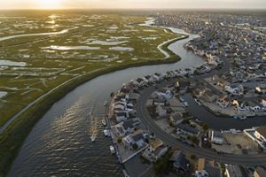 Aerial view of an expansive housing development alongside a river that flows beside coastal wetlands.