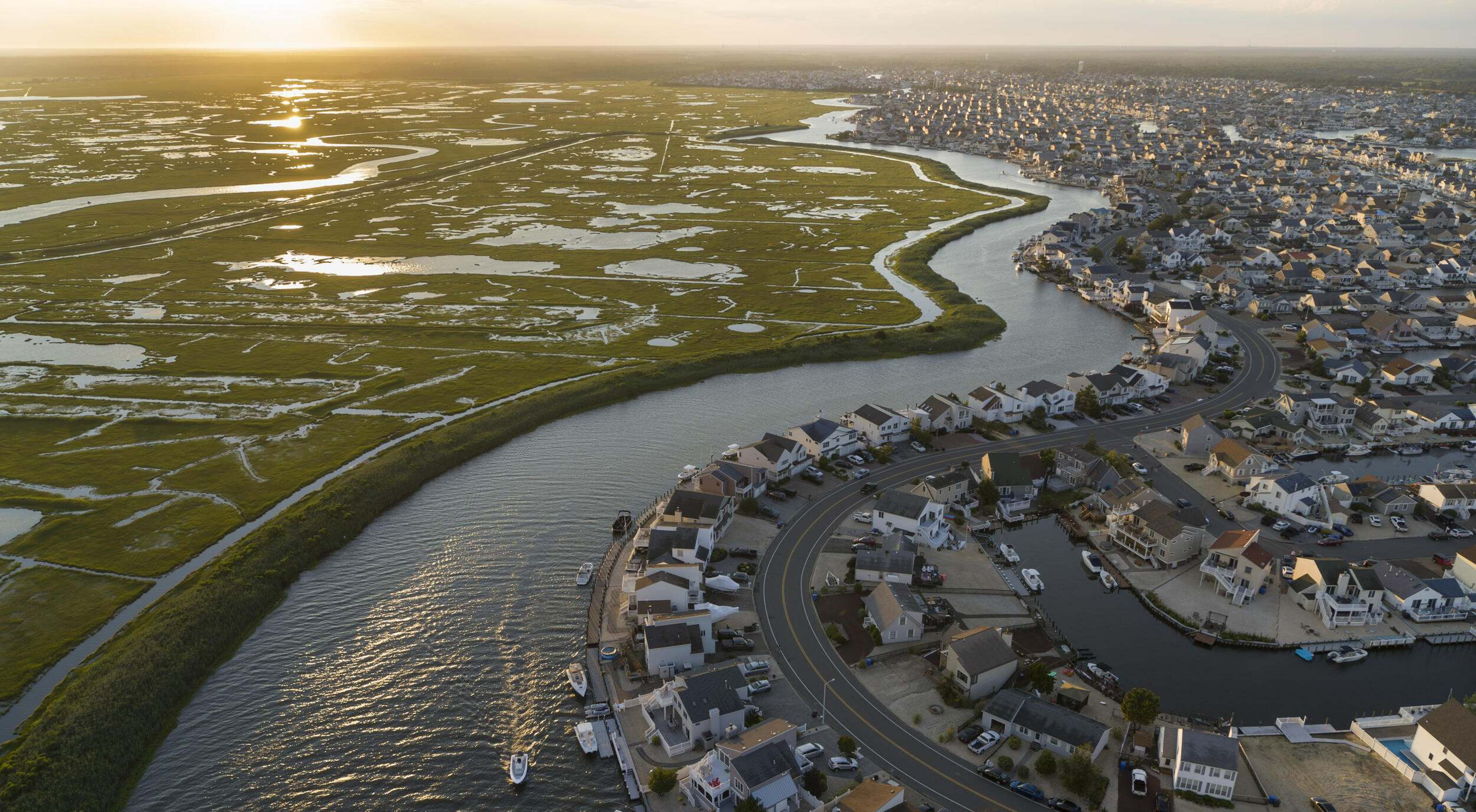 Aerial view of an expansive housing development alongside a river that flows beside coastal wetlands.