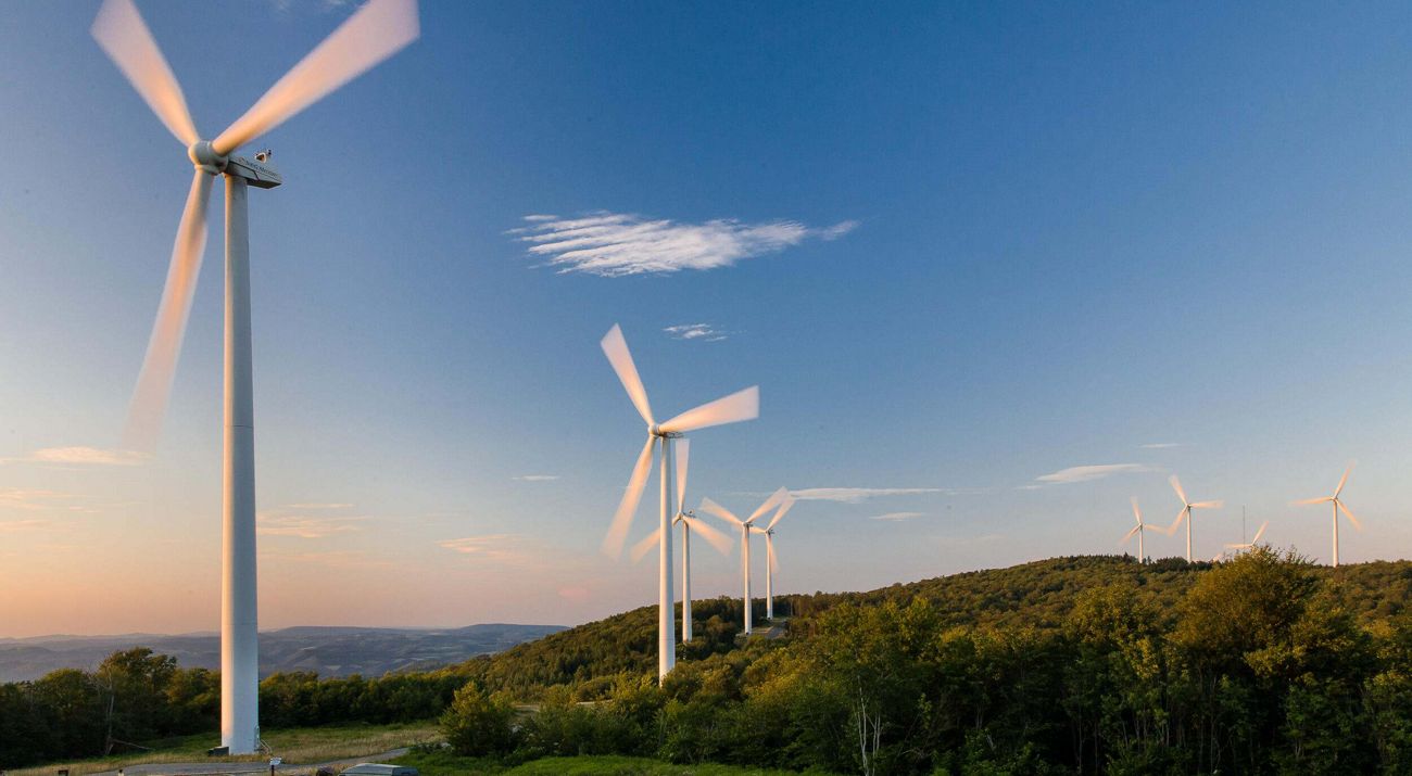 Long exposure image of windmills rotating atop a ridge in hilly terrain.