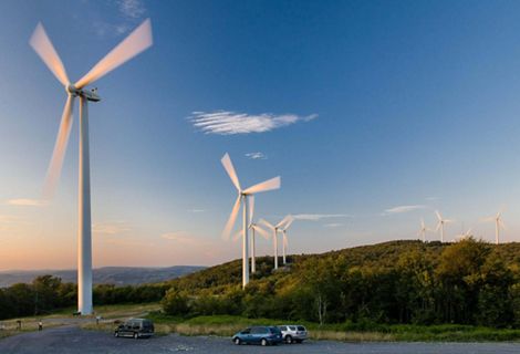 Long exposure image of windmills rotating atop a ridge in hilly terrain.