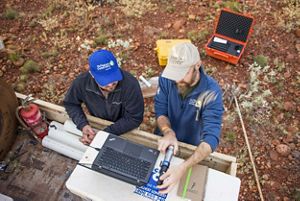 Two staff members wearing TNC hats outdoors while examining data on a laptop computer.