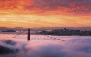 View toward the San Francisco skyline and San Francisco Bay at sunrise with the Golden Gate Bridge peaking through fog that covers it.