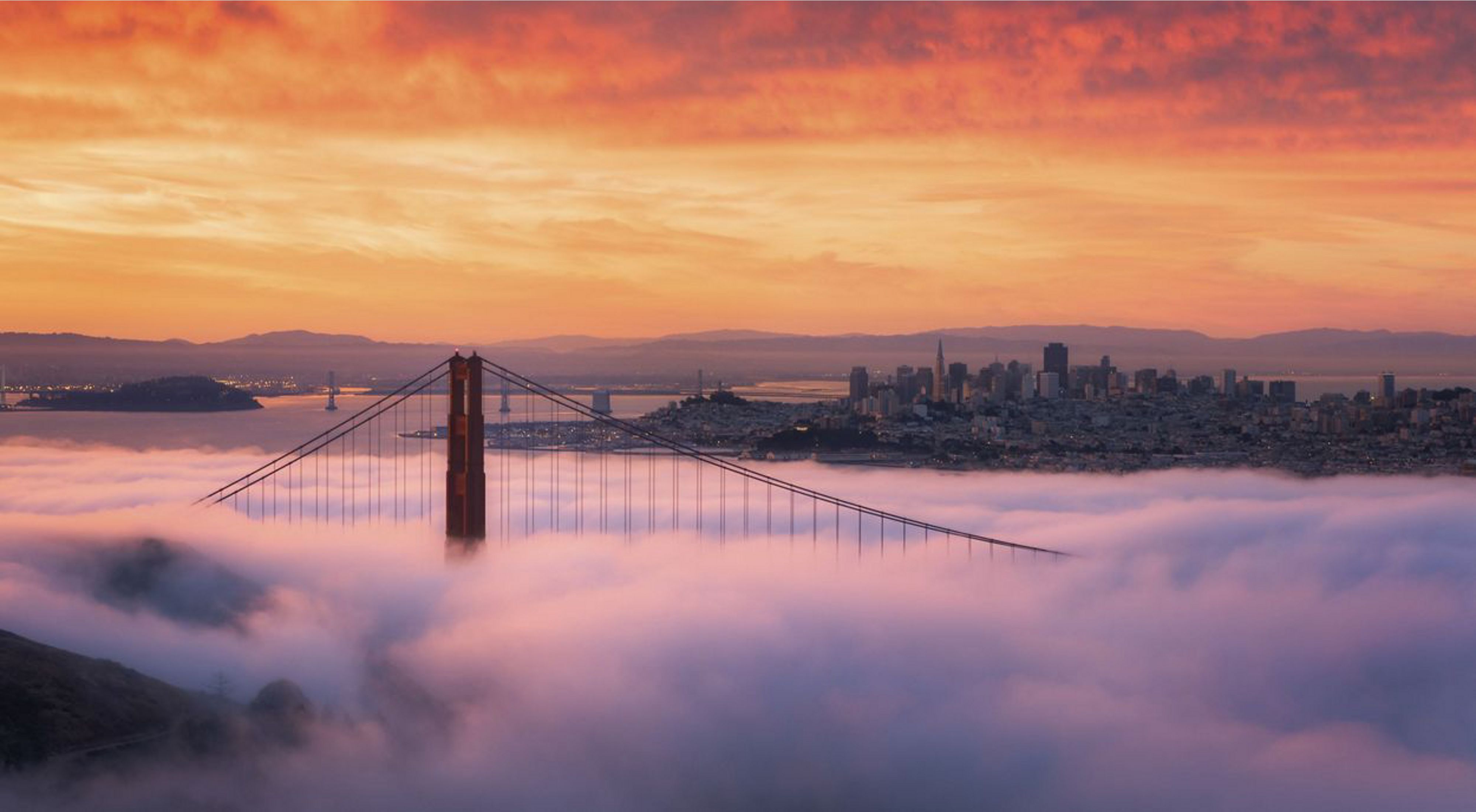 View toward the San Francisco skyline and San Francisco Bay at sunrise with the Golden Gate Bridge peaking through fog that covers it.