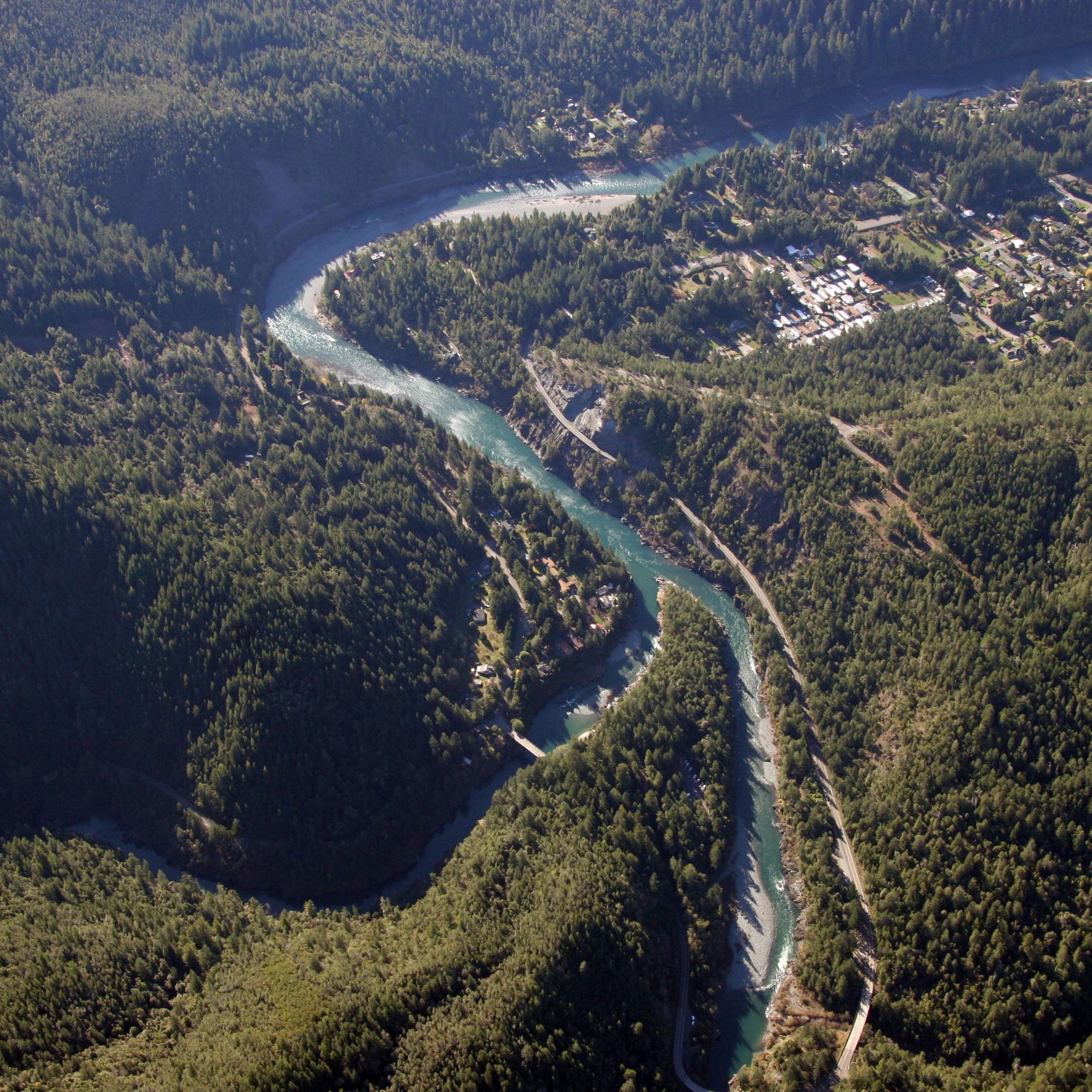 Aerial view of a river meandering through forested mountains with a small town alongside the river.