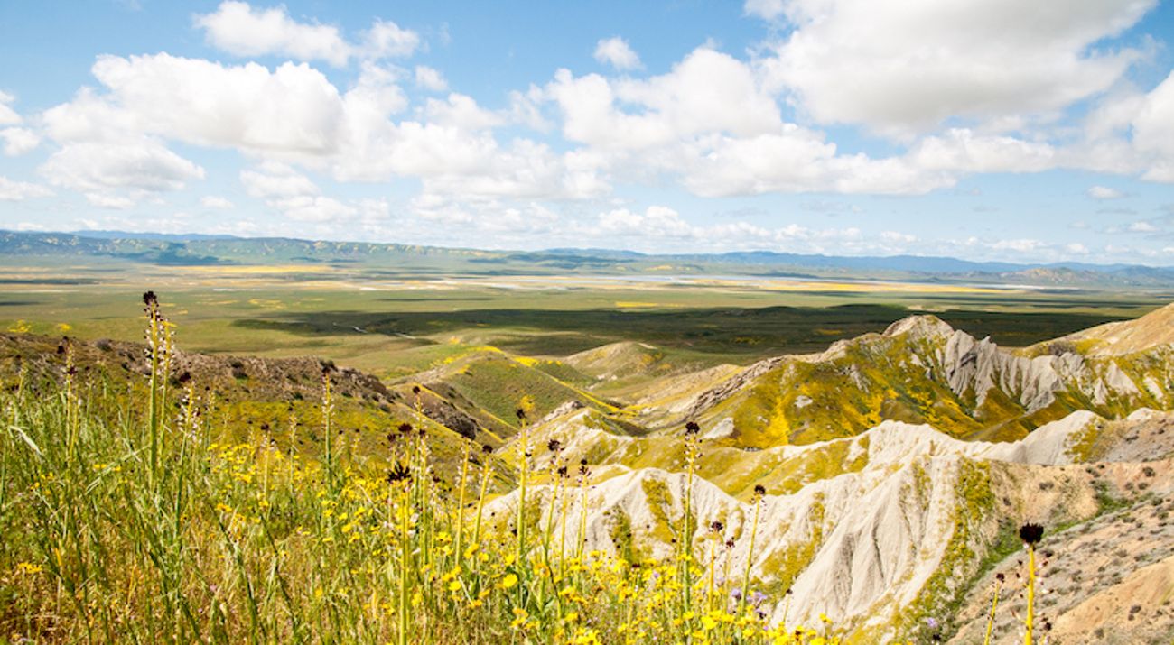 Expansive view of rugged landscape in the foreground with a large plain in the distance.