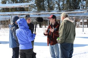 Several people stand in a group around a boom microphone as they record audio for the podcast episode on agrivoltaic renewable energy.