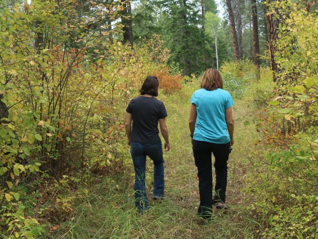 Two women walking through wooded forest.