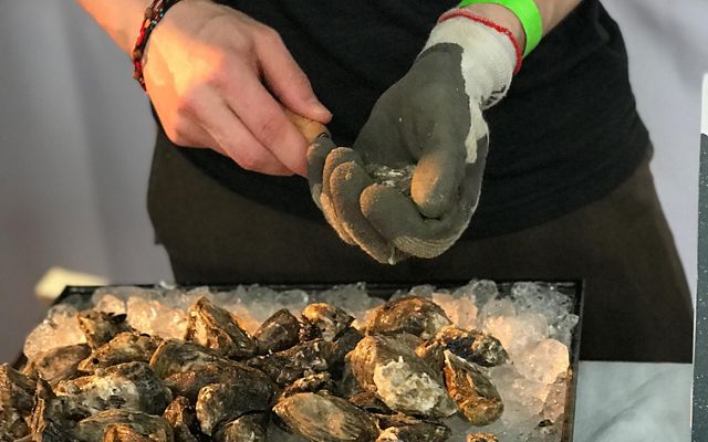 A person wearing a glove shucking oysters.