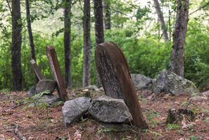 Three reddish headstones propped up by granite stones in a small forest clearing.