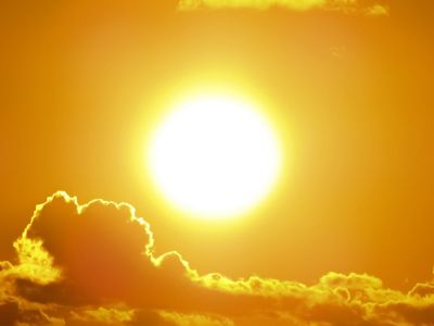 A monochrome view of the sun against clouds in the sky.