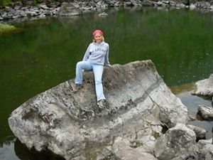 Woman sitting on a large boulder with an expanse of water behind her.