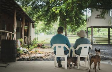 Two people sit in chairs on patio with dogs.