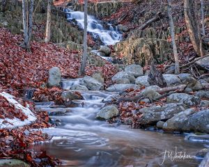 Waterfall and rocky stream surrounded by fallen leaves.