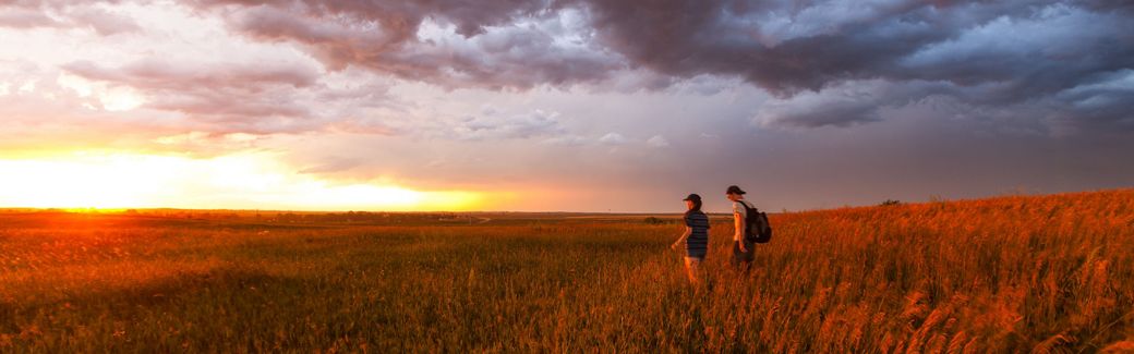 Two hikers walking in a prairie toward the setting sun.