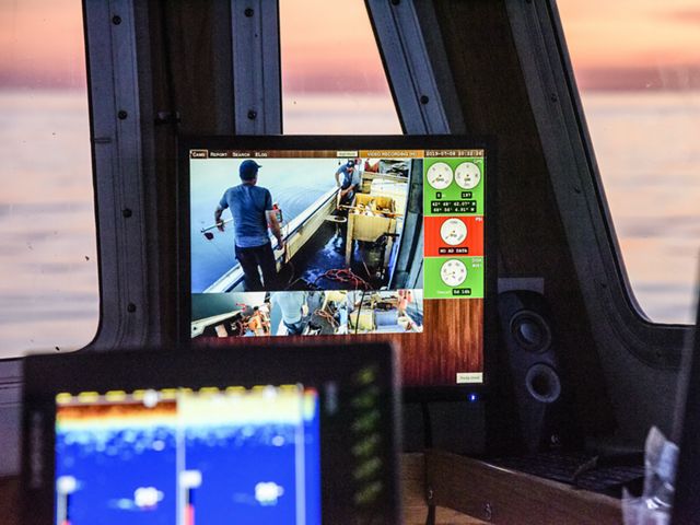 Looking at a monitor inside a fishing boat cabin that shows fishermen at work on the deck.