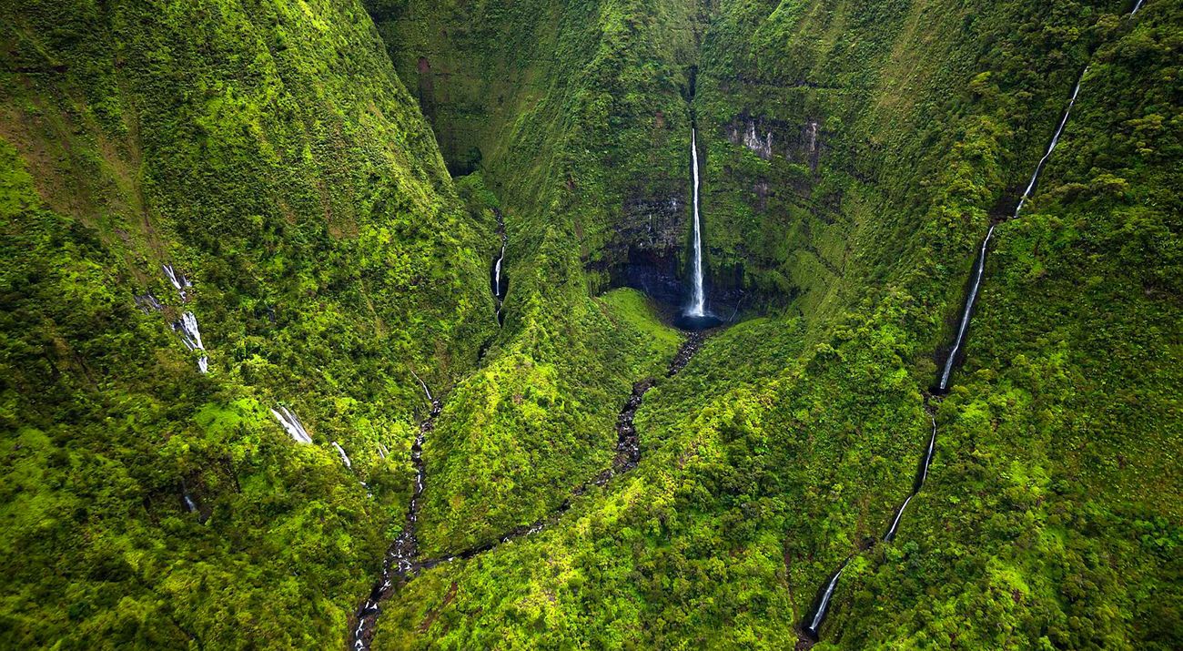A waterfall spills down into a deep gorge in a lush canyon of deep green walls.