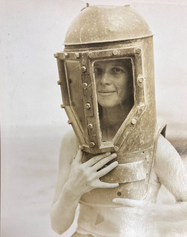 A person wearing a vintage metal diving helmet holds the sides with both hands.