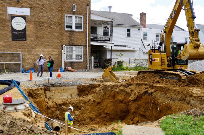 View looking down into a large dirt hole in a parking lot with construction workers inside.