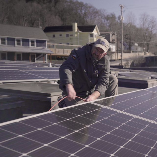 A man checks solar panels on a rooftop.