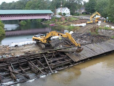 Heavy machinery remove wooden timbers from an old dam in a river.